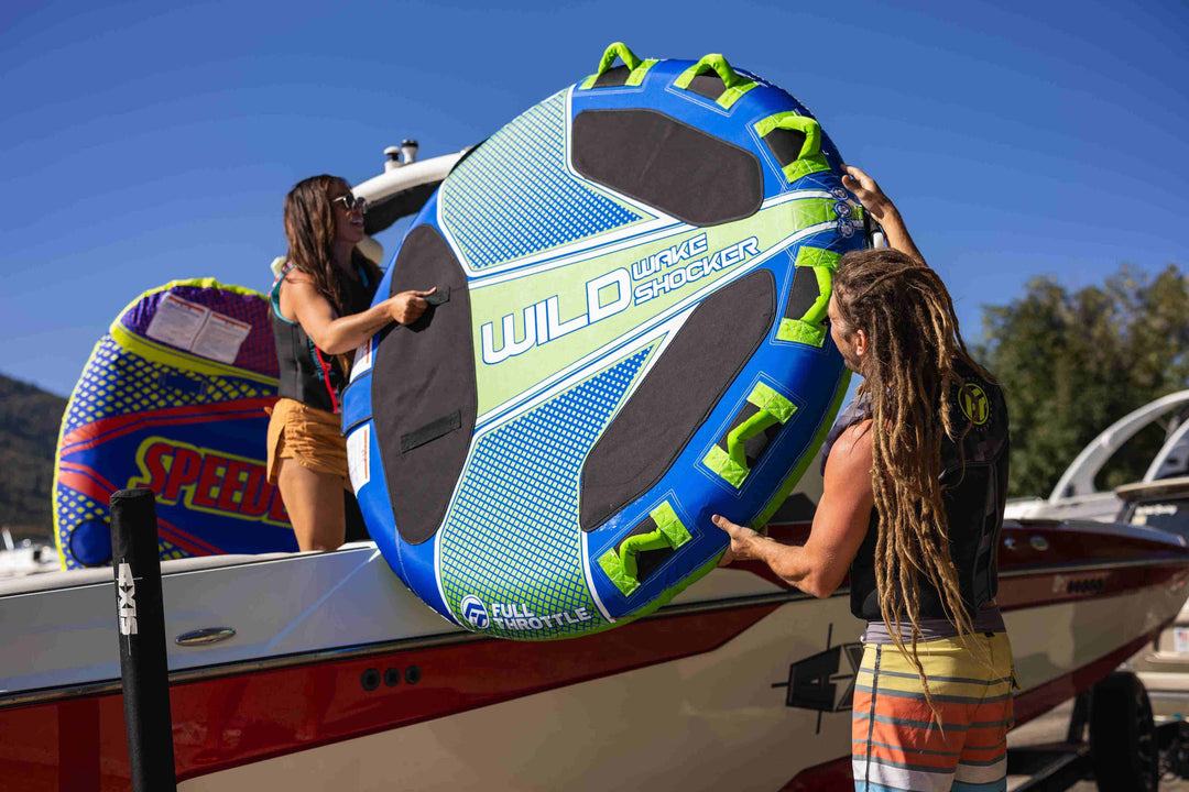 Two people load a towable tube onto a boat.
